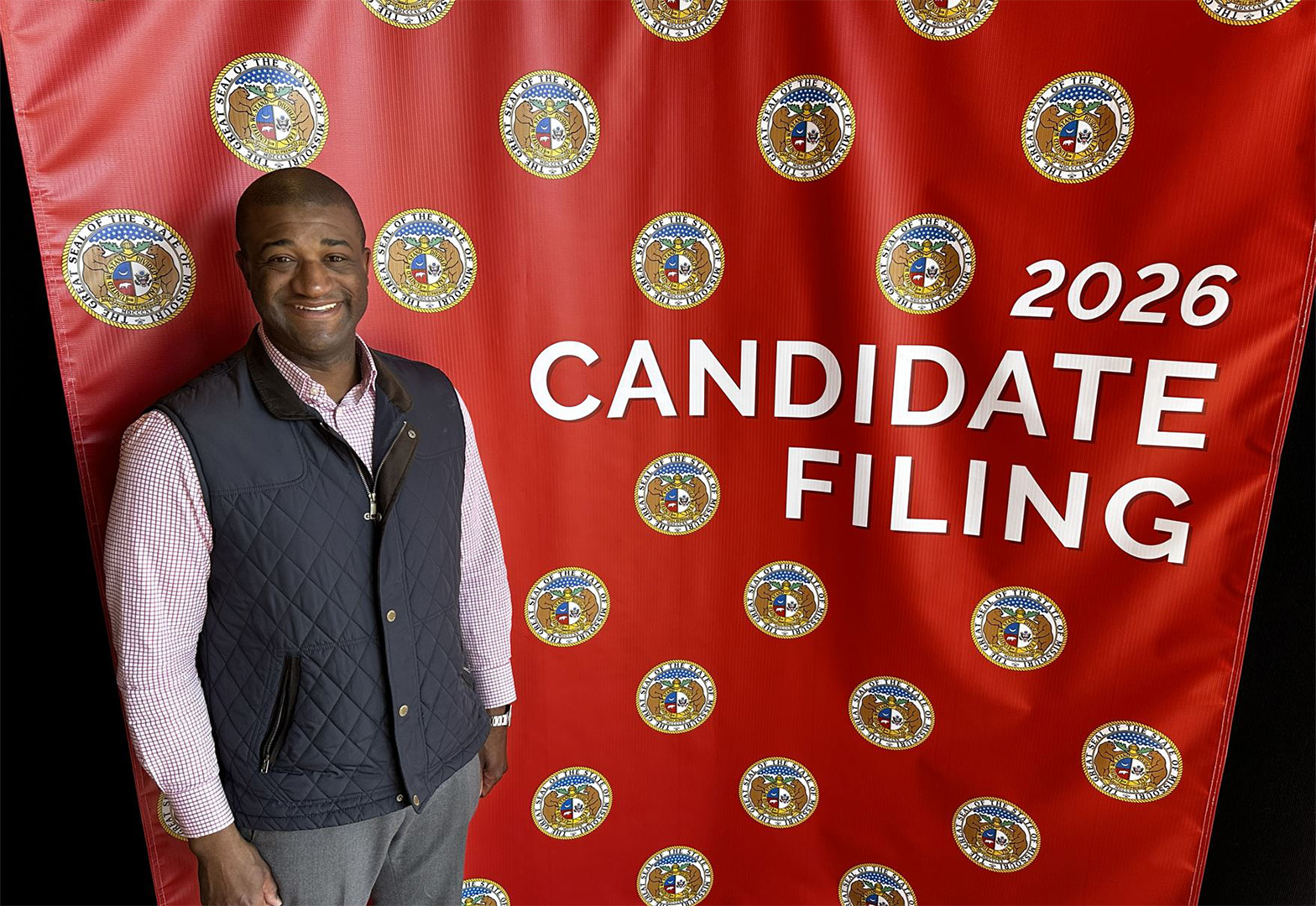 Vernon Norman standing in front of a backdrop containing the seal of Missouri