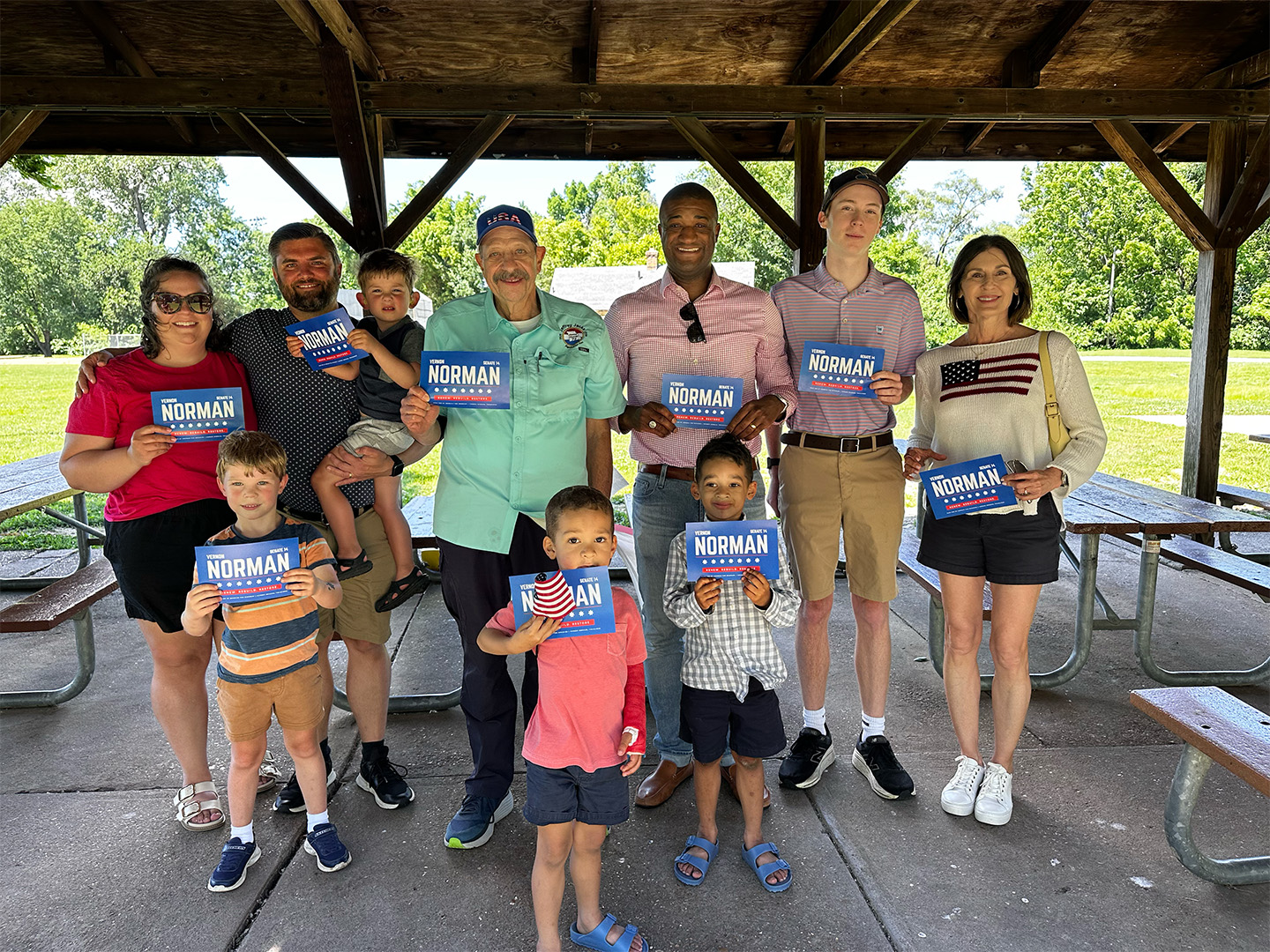Vernon Norman standing with constituents of various ages, from children to adults, holding signs that read Vernon Norman Senate 14